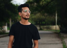 Portrait of a young man wearing glasses, standing outdoors in a park. Casual and relaxed setting.