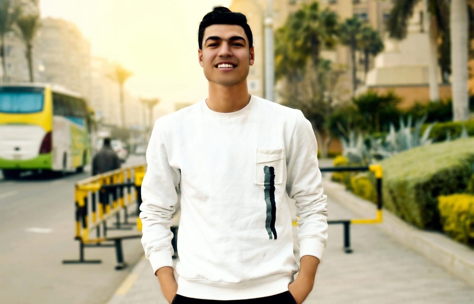 Smiling young man posing confidently on a city street during the day.